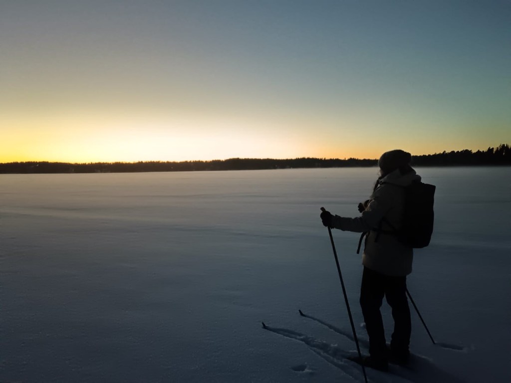 Hiihtäjä ihailemassa auringonlaskua järven jäällä helmikuussa.