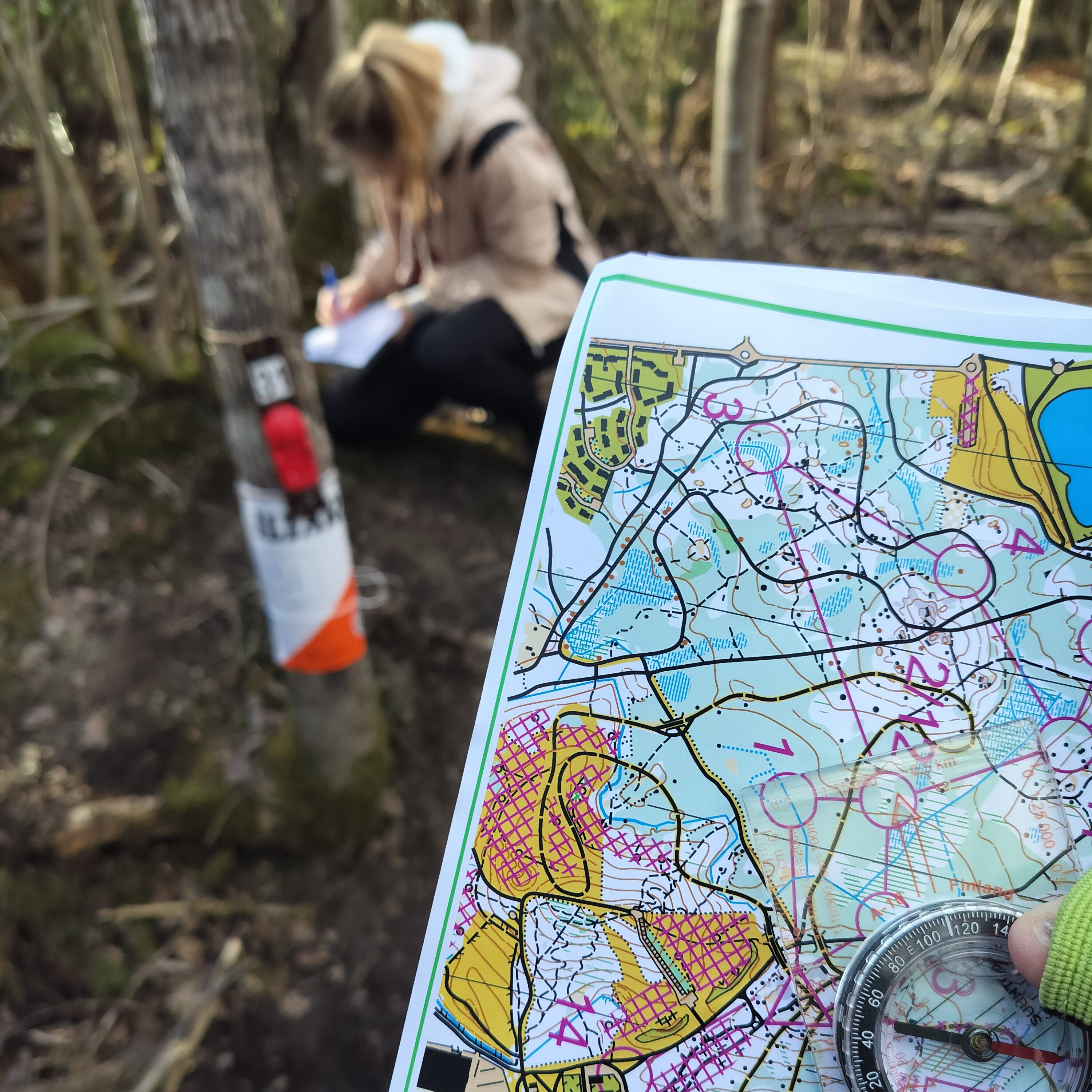 Kuvassa kartta ja kompassi, joiden takana henkilö suunnistusrastilla.