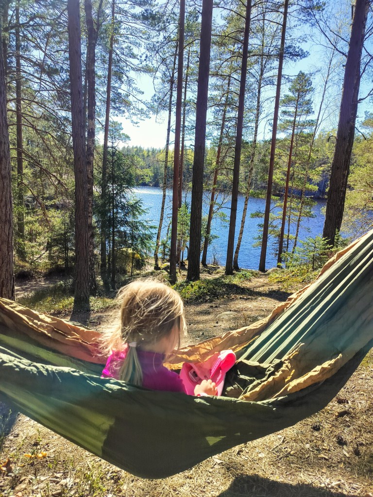 Lapsi istuu riippumatossa järvimaisema taustalla.