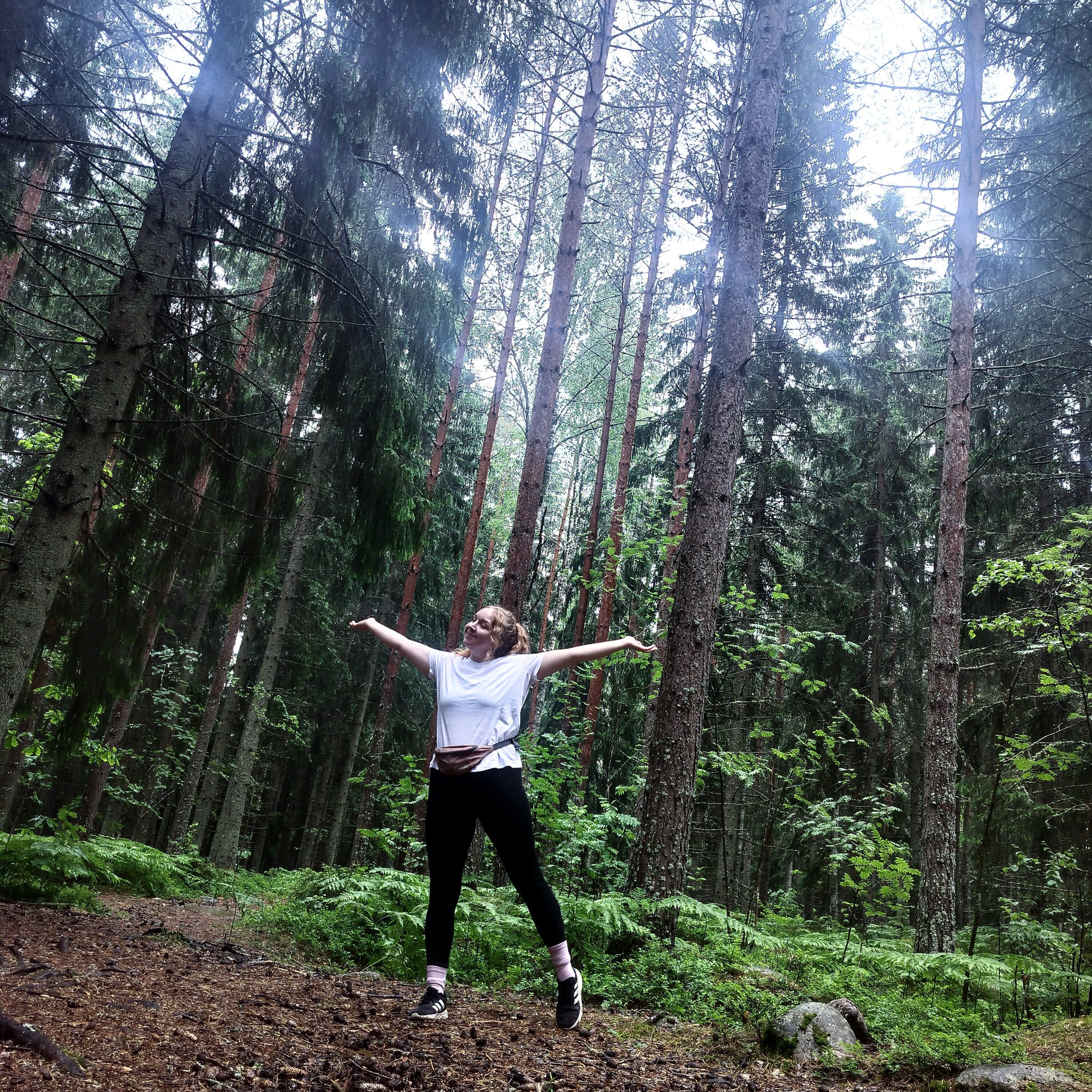 Nainen seisoo onnellisen näköisenä sateisessa metsässä juoksuvaatteissa