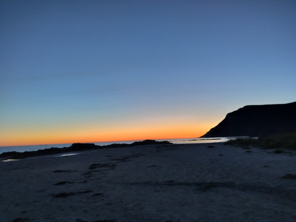Kaunis auringonlasku rannalla vuorimaiseman edessä.